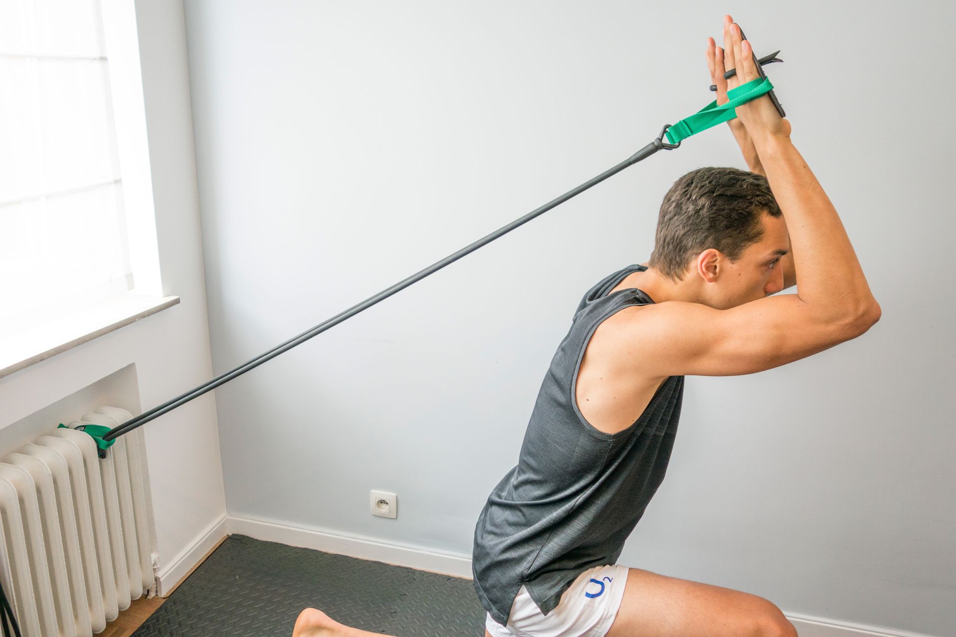 An athlete in a lunge, hands in the paddles of a green FEROK PRO cord that is looped around a radiator